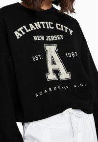 Sudadera negra con un gráfico de estilo vintage. El texto dice "Atlantic City, Nueva Jersey, EST. 1967, BOARDWALK, A.C." en blanco. Diseño recortado.