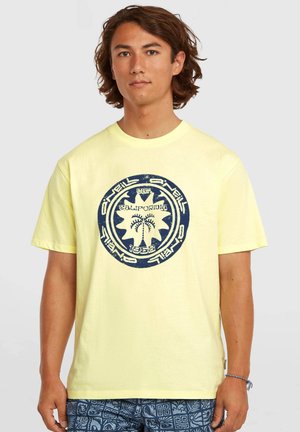 Gul bomuld T-shirt med en cirkulær blå grafik med palmetræer og tekst. Kortærmet og rundhals.