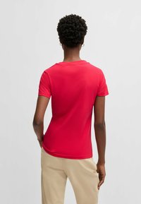 T-shirt rossa a maniche corte con collo rotondo, realizzata in tessuto morbido, silhouette aderente, texture liscia, abbinata a pantaloni beige chiaro.
