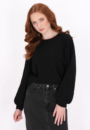 Top nero a maniche lunghe con scollo rotondo e maniche a sbuffo, abbinato a una gonna di jeans nera a vita alta, con uno spacco anteriore.