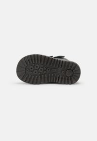 Suela de zapato de goma negra con patrones hexagonales y acanalados para mayor agarre, con una textura sólida y resistente y una forma de punta redondeada.