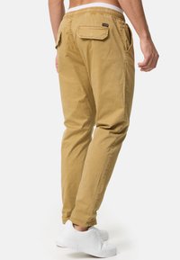 Pantalones caqui de corte relajado, con cintura elástica, dos bolsillos traseros y un diseño de pierna ajustada. Combinados con zapatillas blancas.