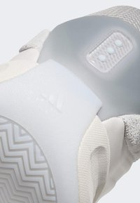 White athletic shoe with a textured upper, translucent heel panel, and three small LED indicators. Features a patterned rubber sole.