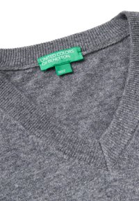 Szary sweter w splot wełniany z dekoltem w kształcie litery V oraz prążkowanym wykończeniem. Posiada zieloną metkę z napisem "UNITED COLORS OF BENETTON", wyprodukowany w Słowenii.