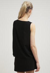 Top senza maniche nero con una vestibilità rilassata, caratterizzato da un collo rotondo e un tessuto morbido e leggero. Design semplice senza motivi visibili.