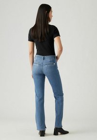 Vaqueros de mezclilla azul claro con corte recto, detalles en los bolsillos traseros y una textura suave, combinados con una camisa negra ajustada.