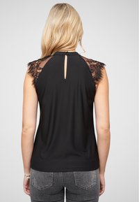 Haut sans manches noir avec des accents en dentelle sur les épaules et un décolleté en forme de goutte d'eau au dos, fabriqué à partir d'un tissu lisse et léger.