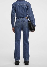 Jeansjacka och högmidjade jeans i mörkblått, med en figurnära silhuett, långa ärmar och bakfickor. Texturerat tyg. Svart väskaccessoar.