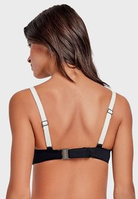 Top bikini nero con spalline bianche regolabili, dotato di chiusura con fibbia metallica sul retro e tessuto elastico e liscio.