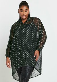 Camicia nera trasparente con bottoni, motivo a pois argentati, maniche lunghe e orlo a barriera. Tessuto morbido e leggero con una vestibilità rilassata.