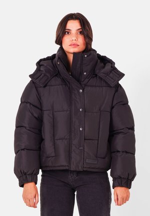 Zwarte pufferjack met hoge kraag, drukknoopsluiting en grote gekwiltte secties. Bevat een capuchon en elastische manchetten voor extra warmte.