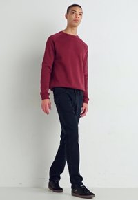 Pulover maroon cu gât rotund, blugi negri și adidași închiși la culoare. Croială casual cu manșete și tiv cu nervuri. Design minimalist, fără modele vizibile.