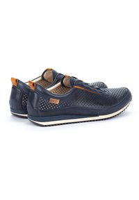 Scarpe slip-on in pelle blu navale con design perforato, dettagli in cuoio chiaro e suola in gomma bianca. La parte posteriore presenta un'etichetta con il logo e cuciture decorative.