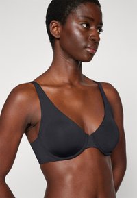 Black bra with molded cups, wide straps, and seamless design. Made from smooth fabric, featuring minimal hardware and clean lines.