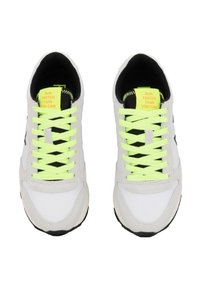 Baskets blanches de sport avec des lacets jaune fluo, des accents noirs et des panneaux texturés. Les semelles intérieures présentent des étiquettes jaunes vives avec du texte noir.