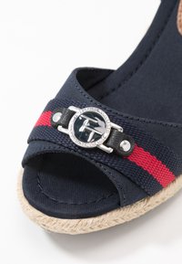 Námořnická látková espadrilková platforma s červeným a černým pruhovaným pásem, disponující stříbrnou kulatou sponou a podrážkou s texturou slámy.