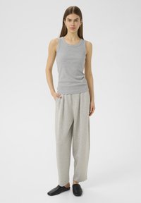 Hallikas ribaga tank top, mis on seotud lõdva halli pükstega. Mudel kannab musti slip-on jalatseid, käed on taskutes, taust on ühtlane valge.