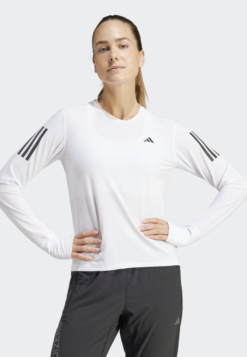 Długi rękaw sportowa koszulka w kolorze białym, z fakturowanej tkaniny, okrągłym dekoltem i trzema czarnymi paskami na każdym ramieniu.