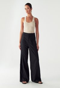 Bež ribana majica bez rukava u kombinaciji s crnim širokim hlačama. Hlače imaju prednje šavove i visok struk. Jednostavne crne sandale.