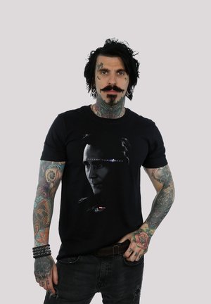 Black cotton T-shirt featuring a graphic of a character's face with the text "Avengers: The Fallen" below, worn by a tattooed individual.