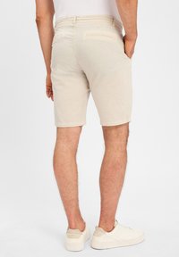 Helle beige Leinenkurze Hosen mit glatter Textur, knielang, mit Gesäßtaschen. Kombiniert mit weißen Sneakern. Einfaches Design, ohne sichtbare Muster.