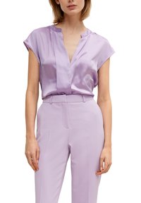 Lavendelfärgad satinblus med korta ärmar, V-ringning och en smidig textur. Matchas med skräddarsydda lavendelfärgade byxor.
