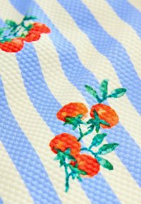 Dekorativt tyg med blå och krämfärgade ränder och strukturerad yta, prytt med livfullt broderade röda tomater och gröna blad.