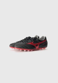 Sorte fodboldstøvler med et strømlinet design, der har røde detaljer og tekstureret syntetisk materiale. Synlige snørebånd og formede studs på en pink sål.
