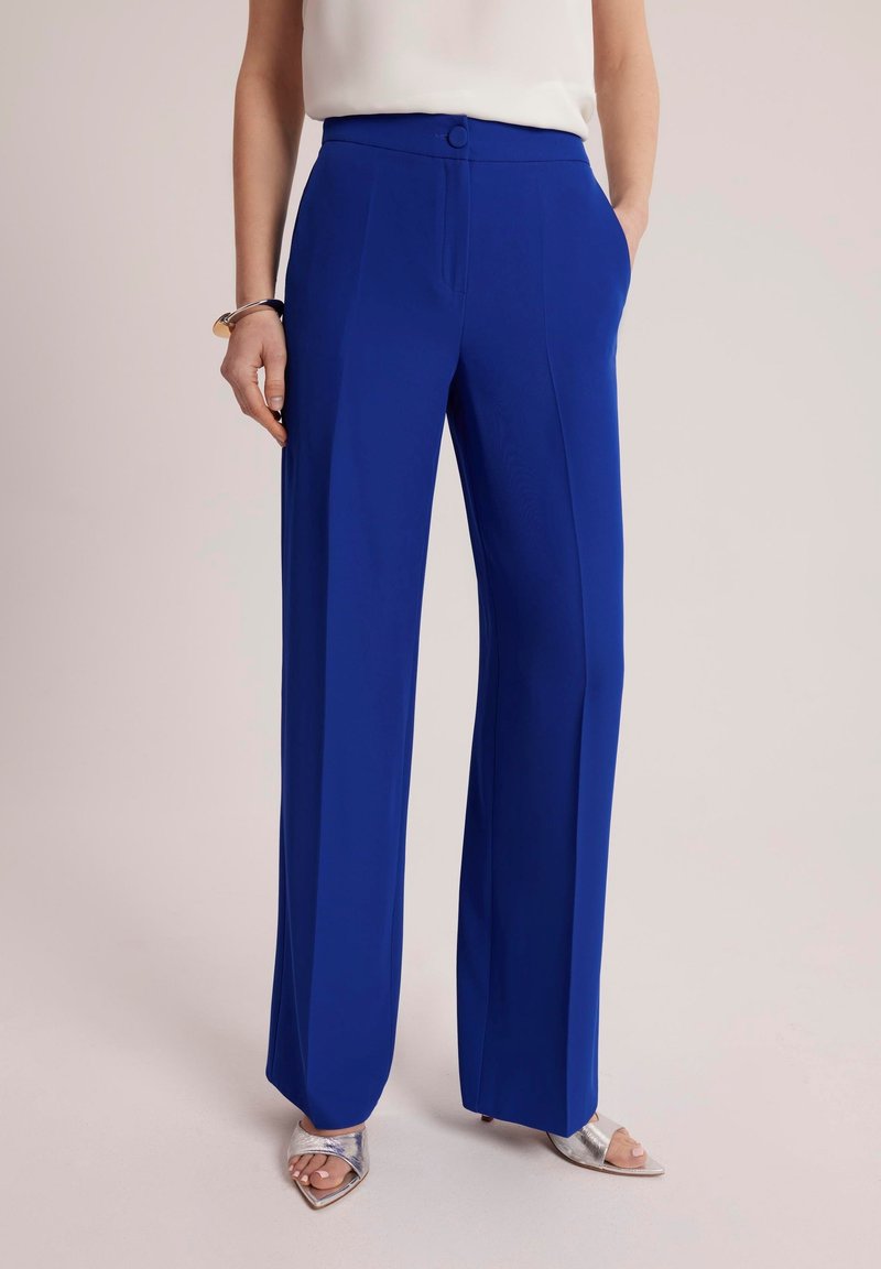 Szerokie, jasnoniebieskie spodnie wykonane z gładkiego materiału. Posiadają wysoki stan, zapięcie na guzik i boczne kieszenie.