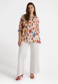 Kolorowa bluzka w wzory z rękawami o długości 3/4, zestawiona z białymi spodniami o szerokich nogawkach i czerwonymi sandałami na wysokim obcasie.