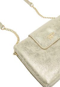 Metaliczna złota torebka crossbody z teksturowanej skóry, z klapką i paskiem z łańcuchowymi akcentami. Posiada logo na przedniej części.