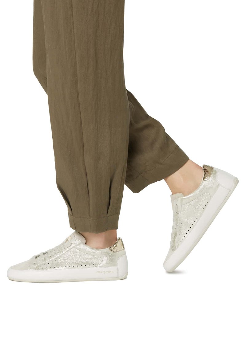 Sneakers with a shimmering silver surface and metallic accents, featuring a white sole and lace-up design, paired with loose olive pants.