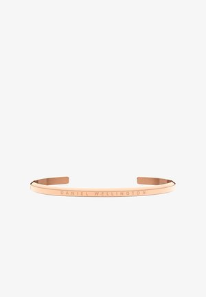Bracelet manchette en métal or rose gravé "DANIEL WELLINGTON" sur la surface extérieure, design ouvert.