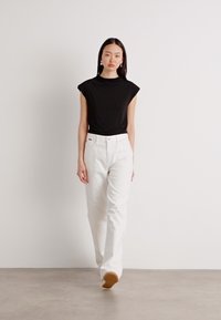 Černý top s krátkým rukávem a vysokým límečkem, doplněný bílými kalhotami širokého střihu s hladkým povrchem a minimalistickým designem.