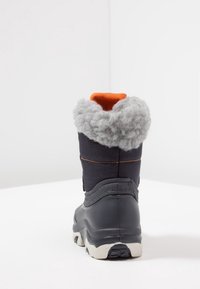 Bota impermeable negra con forro de vellón gris en la parte superior, acento naranja en el cuello, suela texturizada y base resistente de goma.