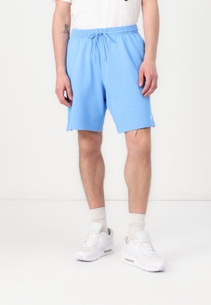 Shorts bleu clair avec une taille élastique et un cordon de serrage, dotés de poches latérales et d'un léger effilochage à l'ourlet. Portés avec des baskets blanches.