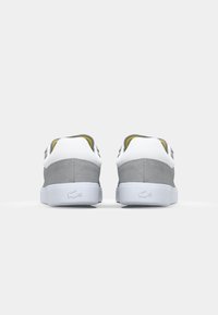 Grijze suede sneakers met een witte rubberen zool. Bevatten een witte hiel en accenten, gele binnenvoering en een reliëflogo aan de achterkant.