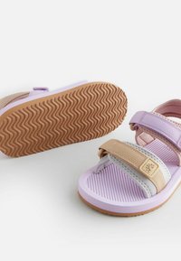 Duos vaikų šlepetės nuošalyje violetinės, rožinės ir smėlinės spalvos, su reguliuojamomis Velcro juostelėmis ir tekstūruotu guminiu padu.