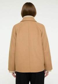 Brun uldblandingsfrakke med en afslappet pasform, der har en ribbet hals og en understated krave. Enkel bagdesignet med minimale syninger.