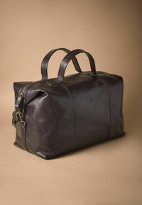 Bolsa de viaje de cuero marrón oscuro con forma estructurada, dos asas resistentes y una correa de hombro desmontable. Cuenta con cierre de cremallera.