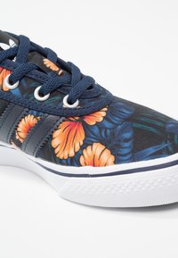 Canvas-sneakers med svart bas som har livfulla orangea blommönster, mörkblå snören och vit gummisula med texturerad detaljering.