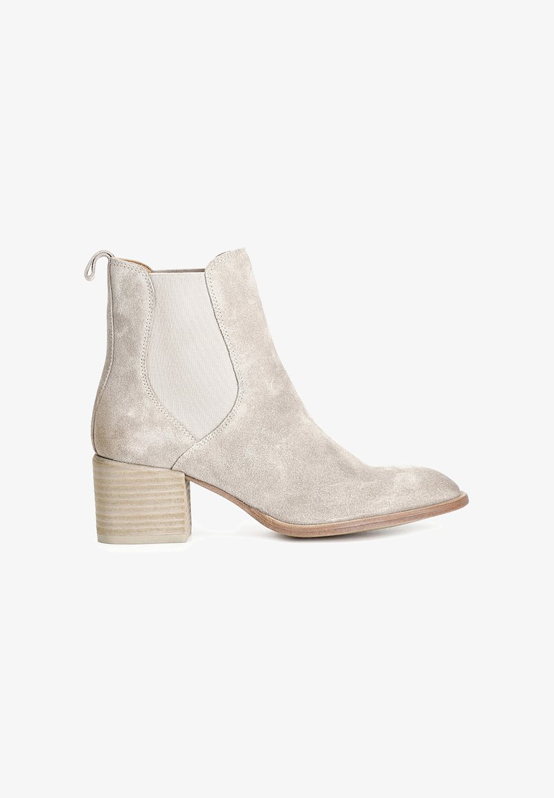 Botín de ante de tobillo en beige claro con punta redondeada, paneles laterales elásticos y un tacón cuadrado estriado. Presenta una lengüeta en la parte posterior.