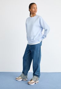 Sweatshirt bleu clair avec col rond, coupe décontractée, associé à un jean en denim ample et des baskets multicolores avec amorti à air.