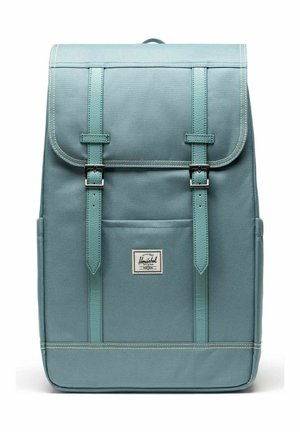 Sac à dos rectangulaire bleu clair avec rabat, deux sangles à boucle, poche avant et étiquette de la marque Herschel centrée sous la poche.