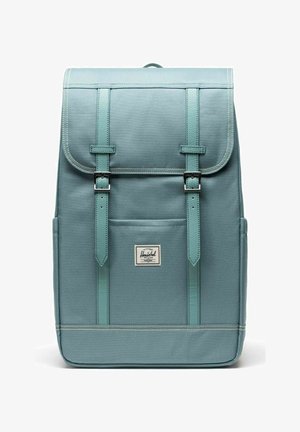 Sac à dos rectangulaire bleu clair avec rabat, deux sangles à boucle, poche avant et étiquette de la marque Herschel centrée sous la poche.