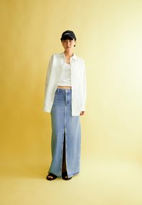 Witte linnen button-up shirt over een cropped geribbelde tanktop, gecombineerd met een high-waisted denim rok met een voorknof en zwarte slippers.
