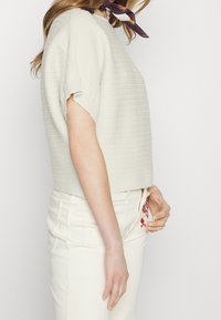 Light gray short-sleeve sweater with a textured rib knit design and a cropped fit, paired with white high-waisted jeans featuring embroidery.