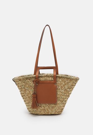 Tkany worek ze słomy z brązową skórzaną rączką, przednią kieszenią i frędzlami, wyposażony w długie paski na ramię oraz prostokątny uchwyt wycięty.