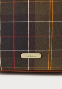 Sötétzöld, barna és fekete kockás anyag vörös és narancssárga részletekkel. Ezüst színű fém címke található rajta, amelyen a "Barbour" felirat olvasható.