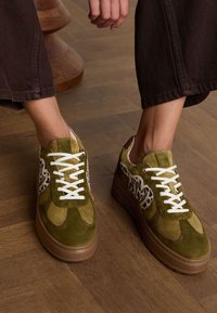 Green suede sneakers with white laces and leopard print accents. Features a thick brown sole and padded collar for comfort.